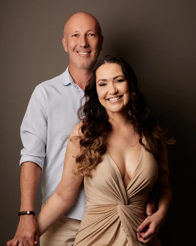 Casal de mãos dadas em ensaio de casal no estúdio, ela de vestido bege e ele de camisa azul clara